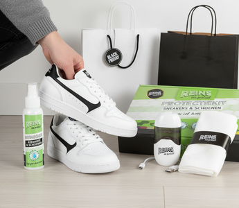 Zwarte vrijetijdssneakers met onderhoudsproducten en Black Friday tasje op de achtergrond.